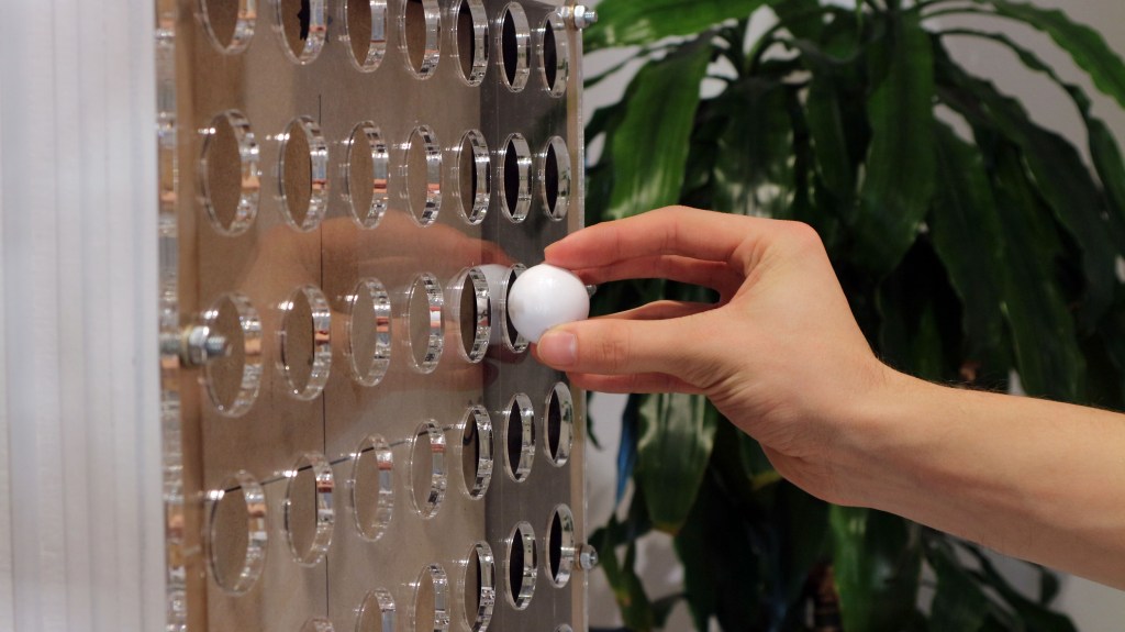 Poster of the M1.1 project, showing a close-up of the prototype in use. A ball is inserted into a grid of holes that represents a quadrant map.