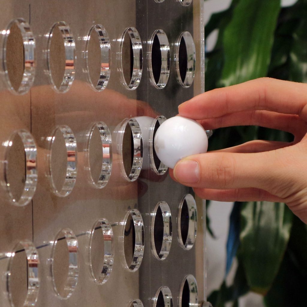 Poster of the M1.1 project, showing a close-up of the prototype in use. A ball is inserted into a grid of holes that represents a quadrant map.